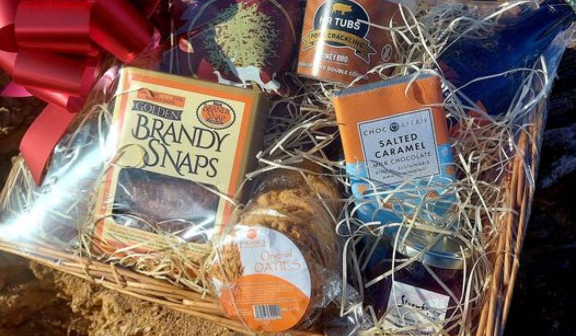 A wooden basket with brandy snaps, chocolate, and other food products inside