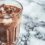 Glass of iced drinking chocolate with chocolate flakes and ice cubes on a marble surface